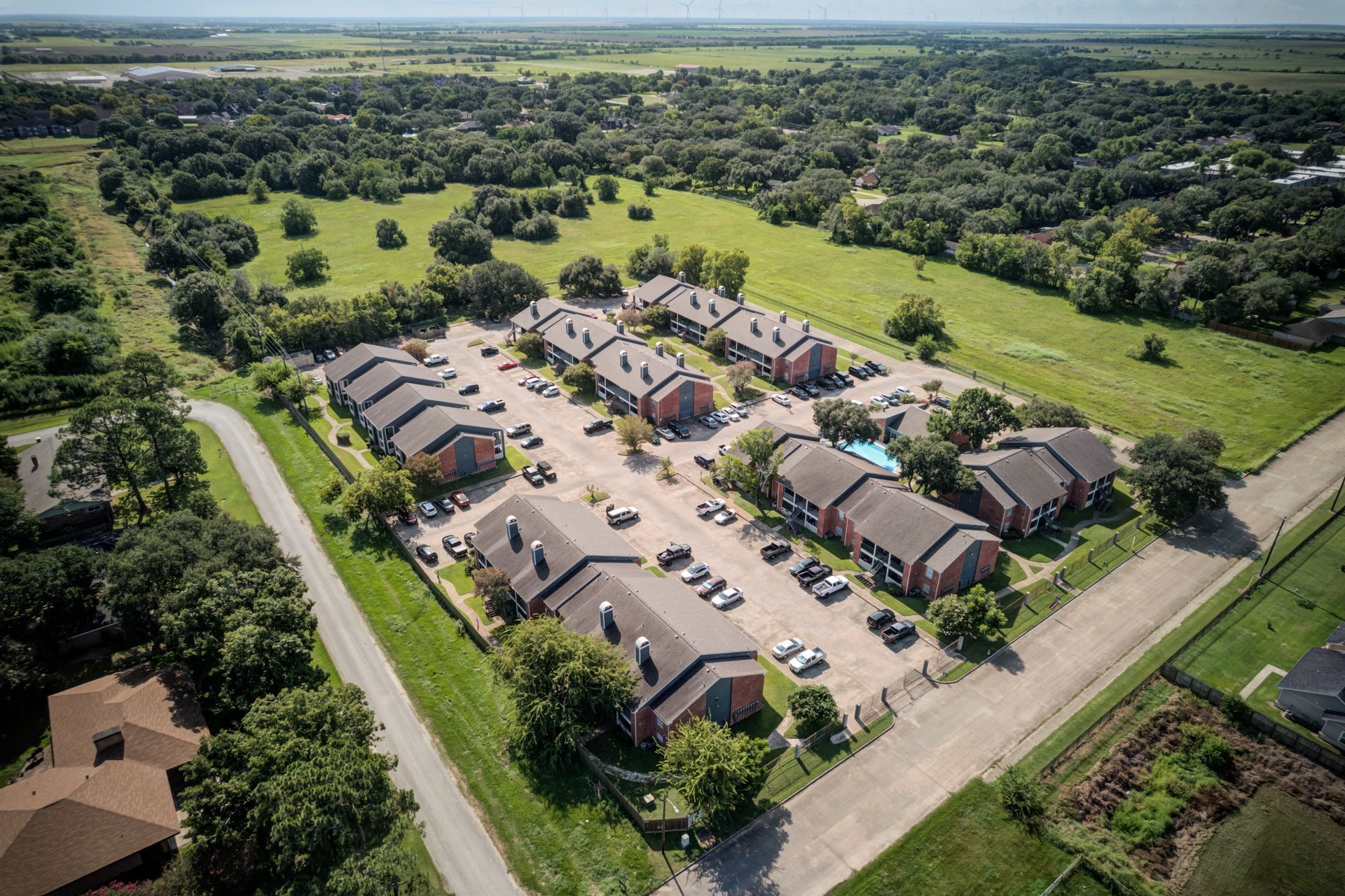 Aerial view of apartment complex with red brick, surrounded by greenery and parking.