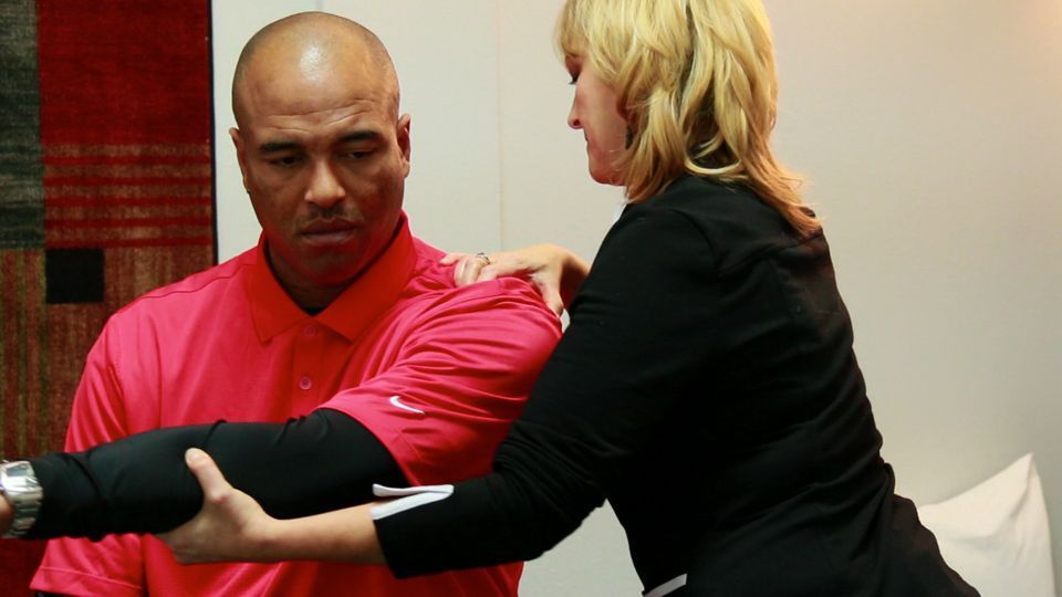 A woman is helping a man stretch his arm