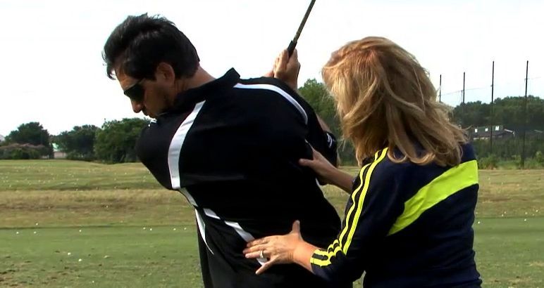 A woman is helping a man swing a golf club