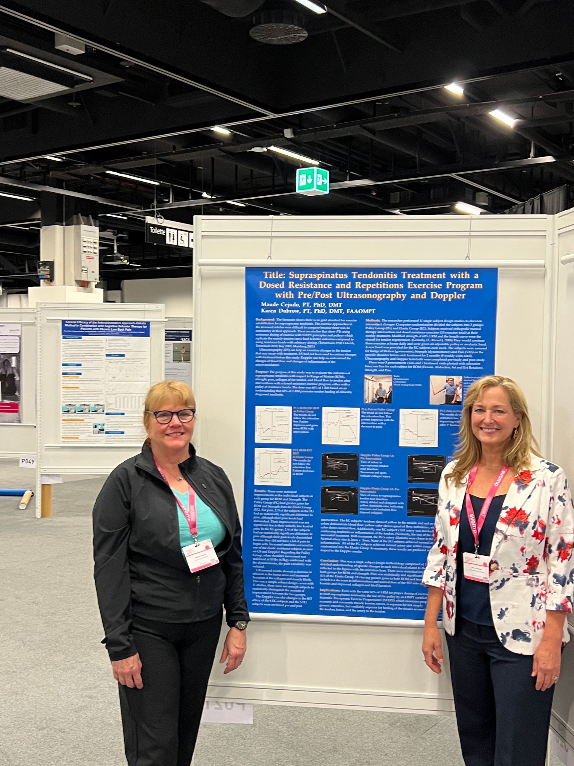 Two women are standing in front of a blue poster on a wall.