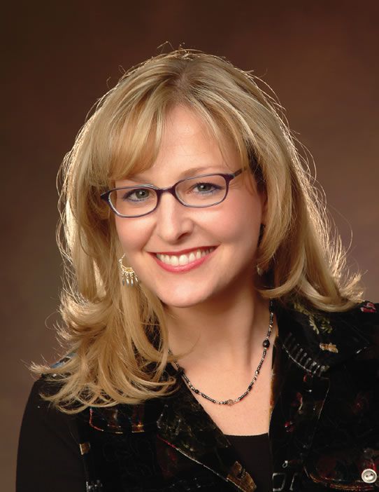 A woman wearing glasses and a necklace smiles for the camera