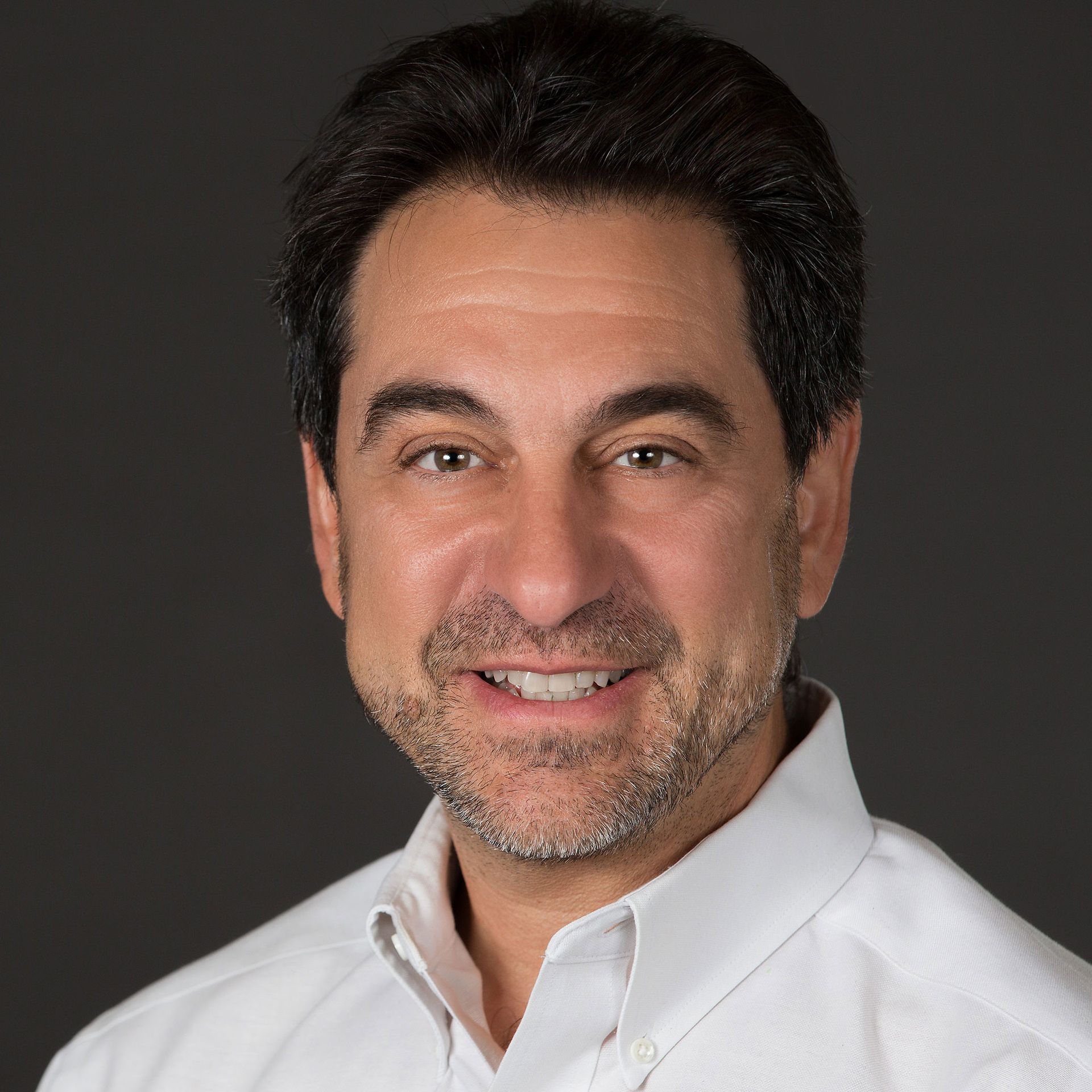 A man with a beard is wearing a white shirt and smiling for the camera.