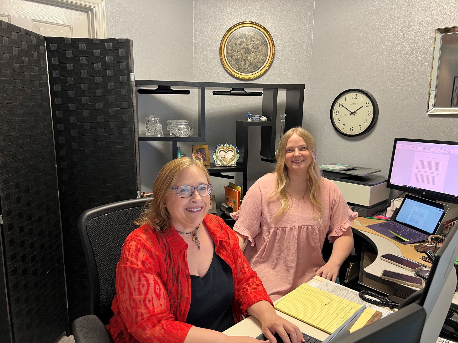 Two women are sitting at a desk in an office.