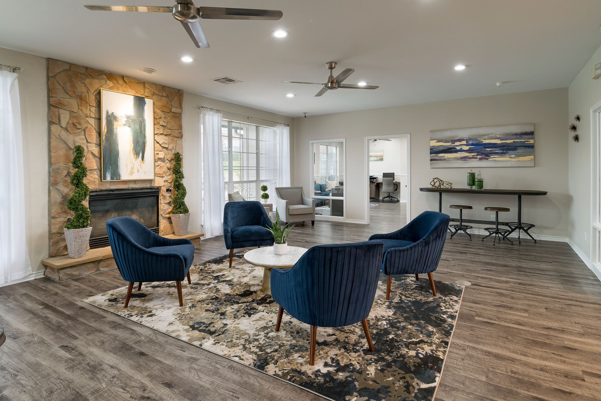 A modern living room with blue chairs, a fireplace, and a large abstract rug.