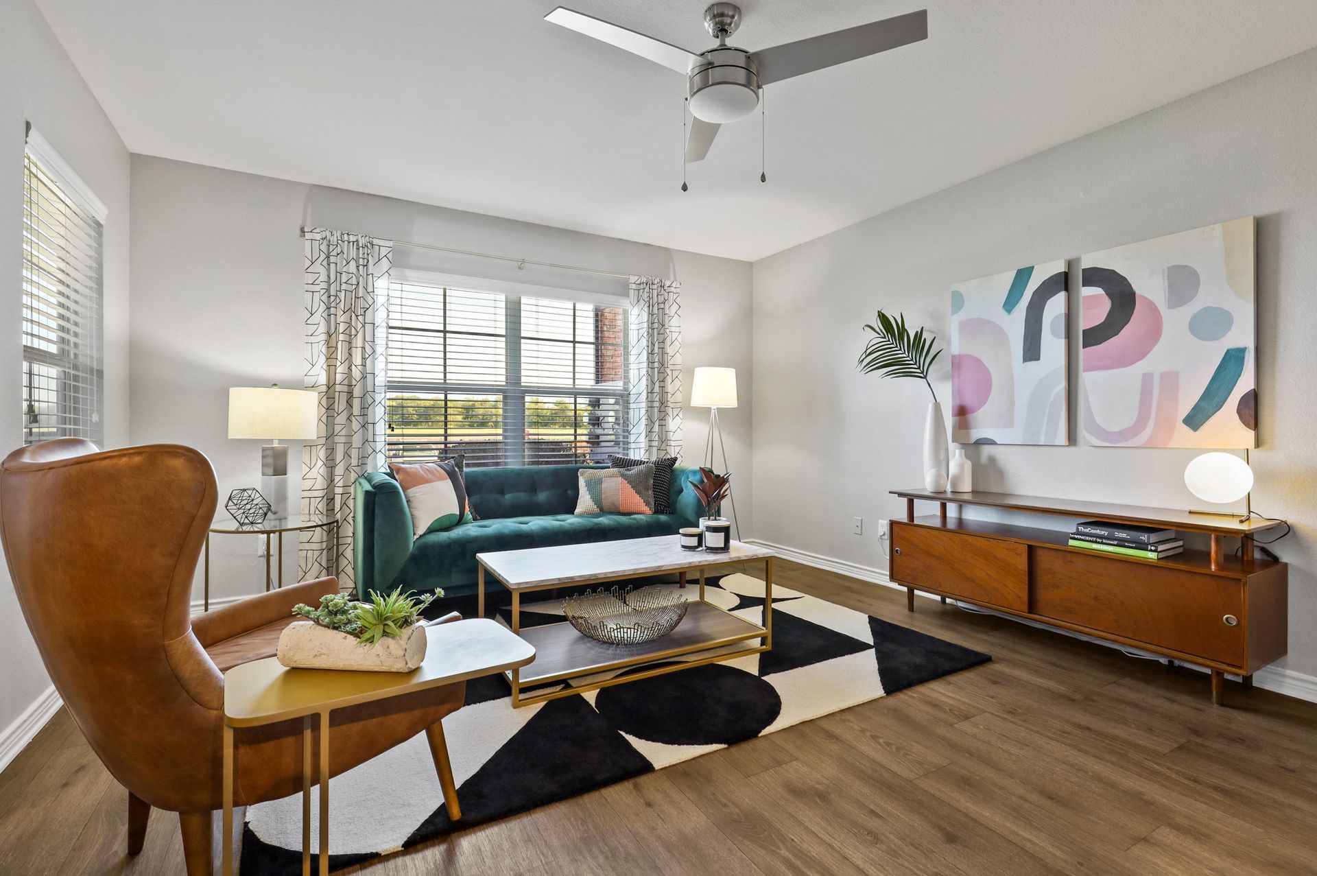 Living room with teal sofa, patterned rug, artwork, and brown leather chair.