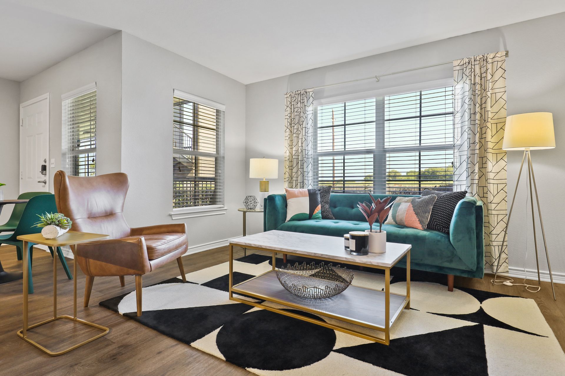 Living room with teal sofa, patterned rug, accent chair, window, and decorative curtains.