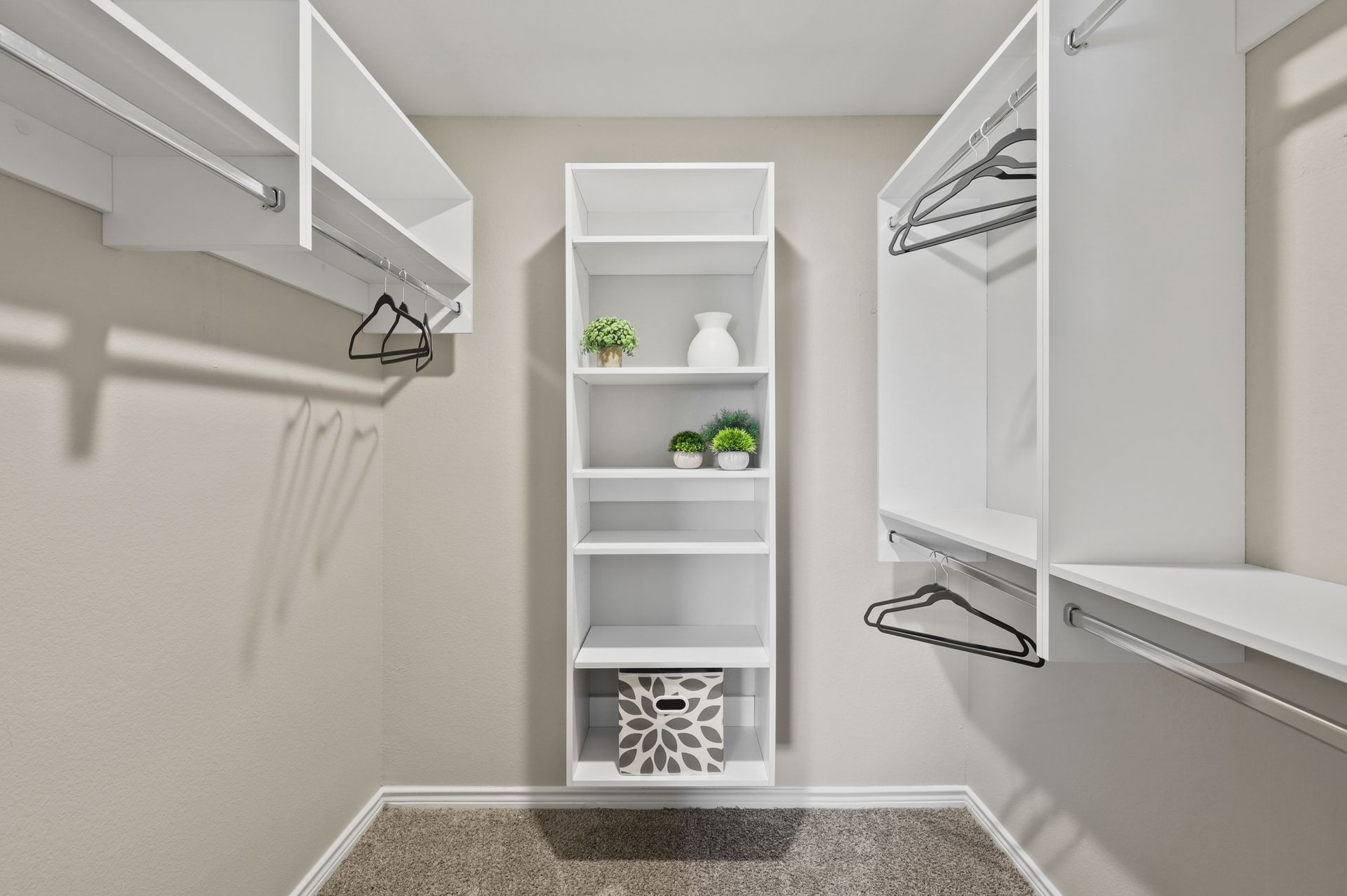 Empty white closet with shelves and hanging rods, neutral walls, carpeted floor.