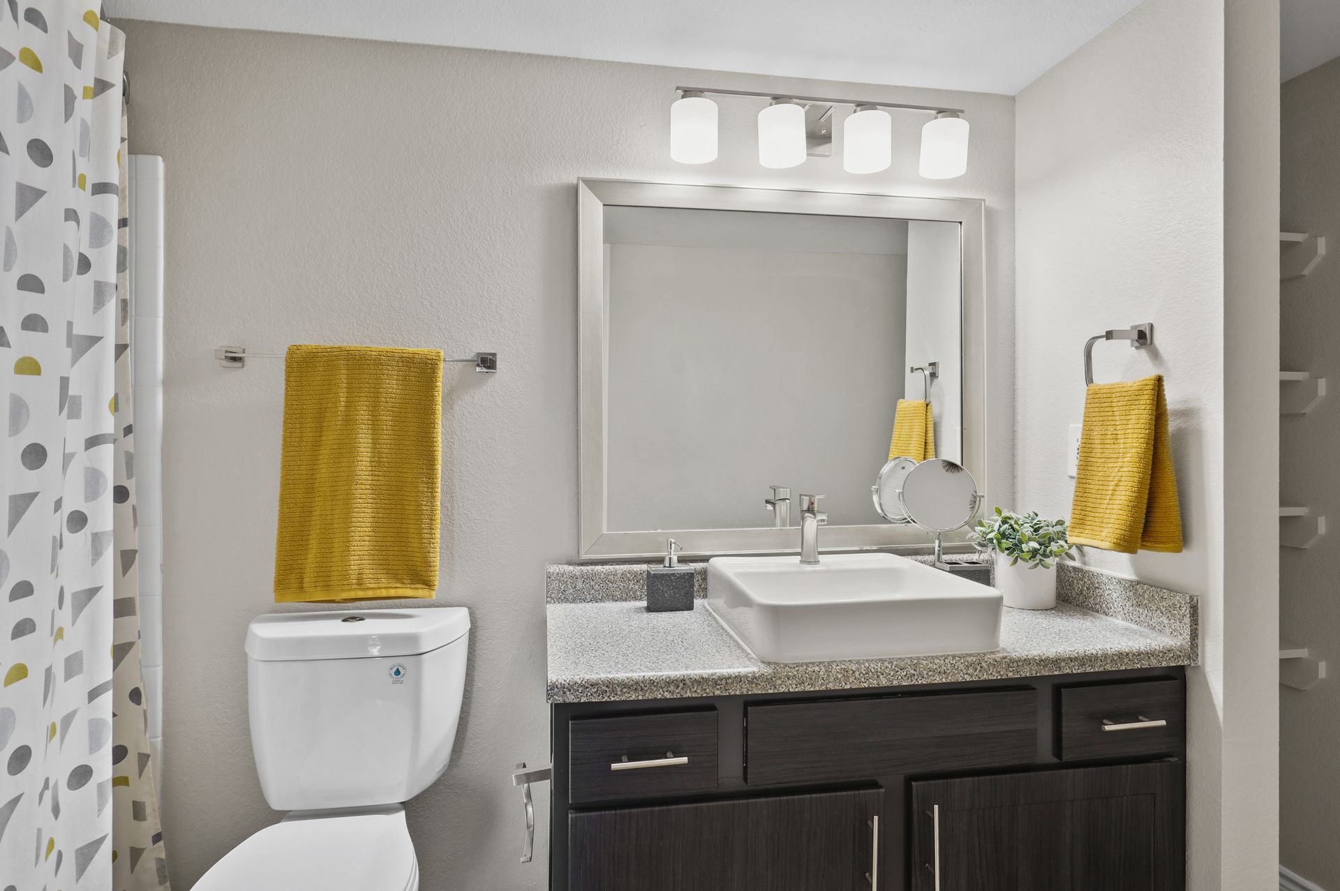 Bathroom with white sink, dark cabinet, mirror, and yellow towels.