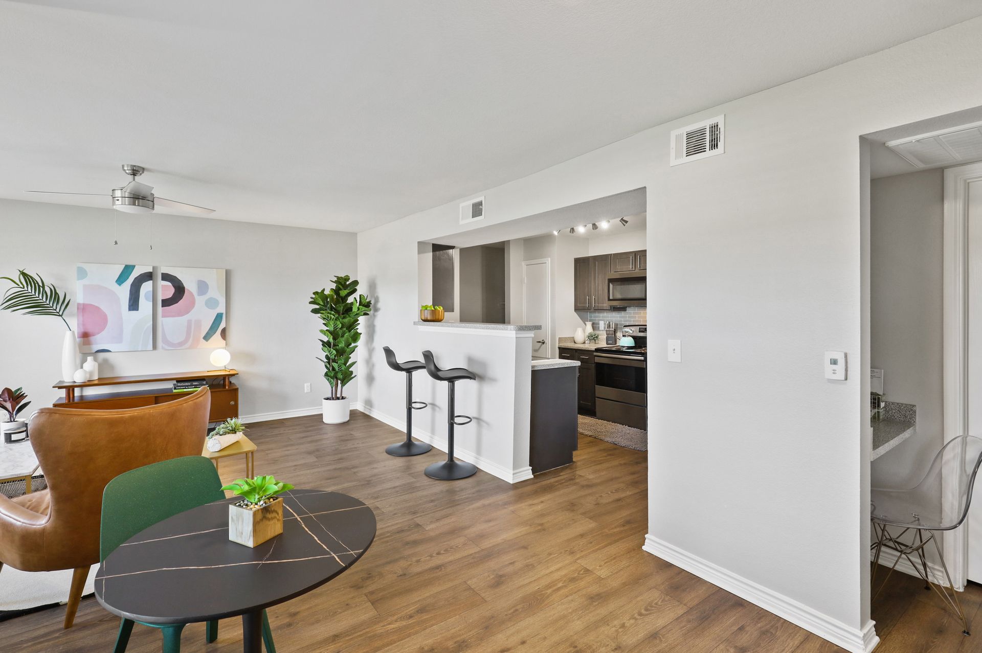Open-concept living space with a dining area, kitchen, and seating area. Dark wood floors and light gray walls.