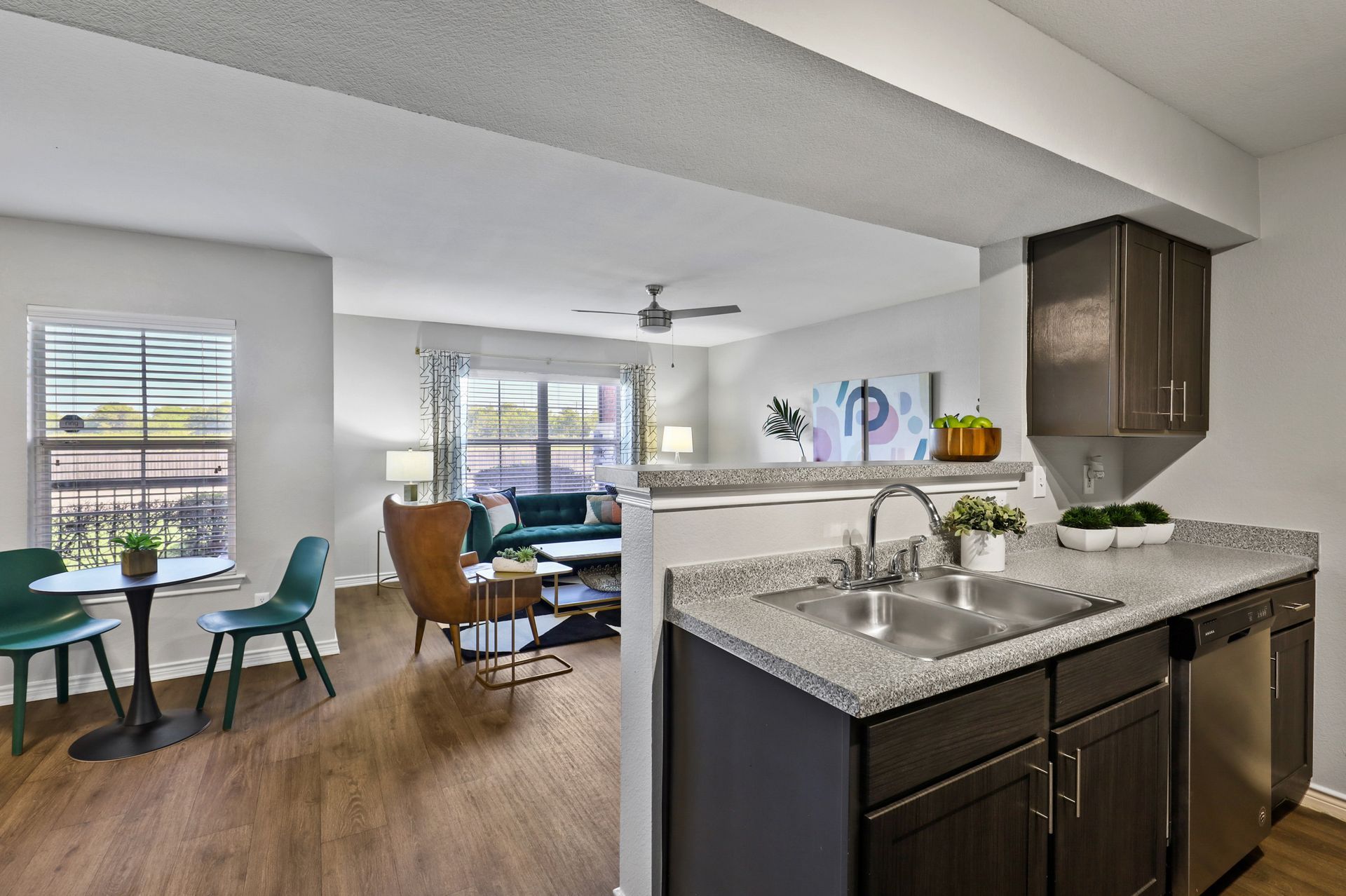 Interior view of an apartment with a kitchen, dining area, and living room; gray and teal color scheme.