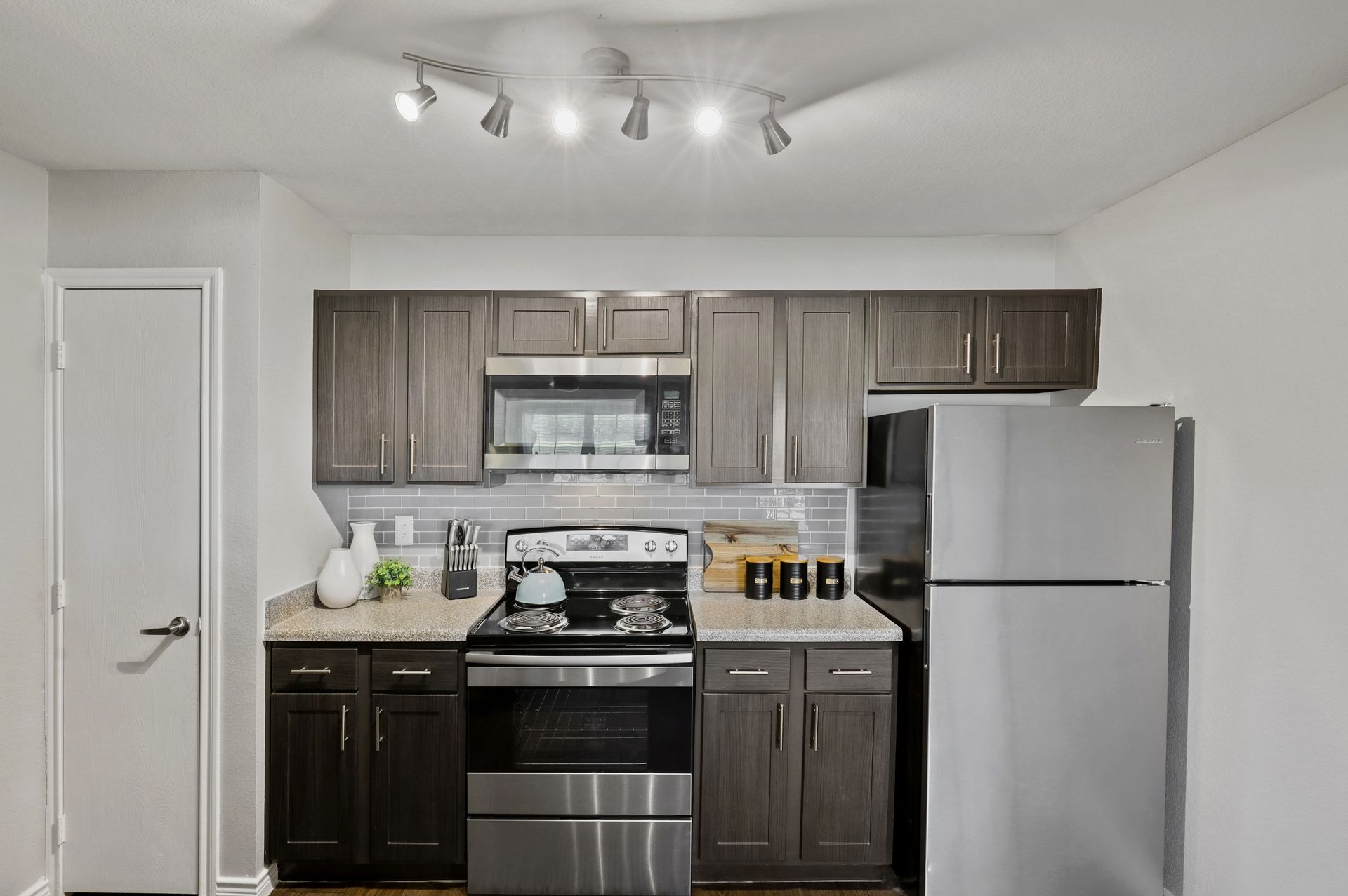 Kitchen with stainless steel appliances, dark cabinets, granite countertops, and track lighting.
