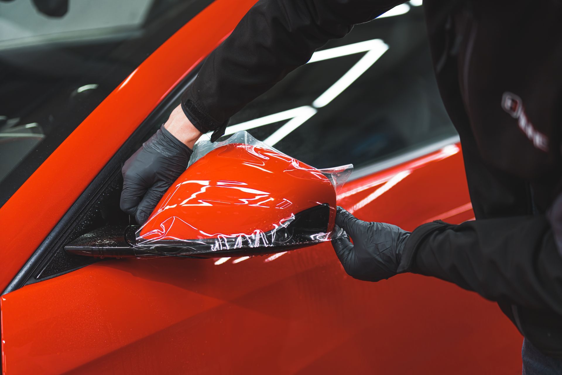 A man is wrapping a side view mirror on a red car.