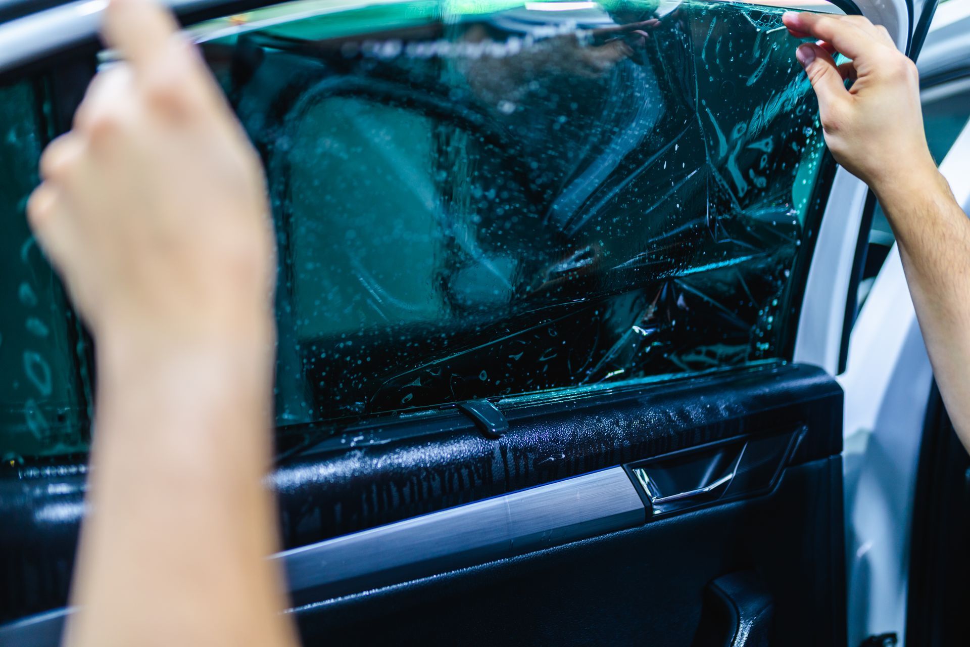 A person is applying tinted window film to a car window.