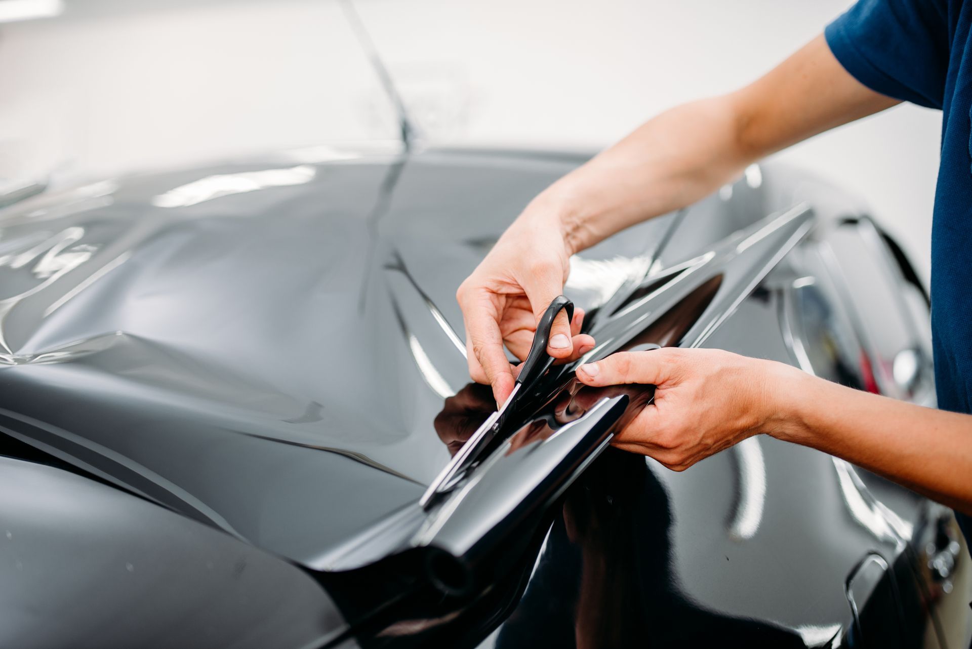 A man is applying window tinting to a black car.