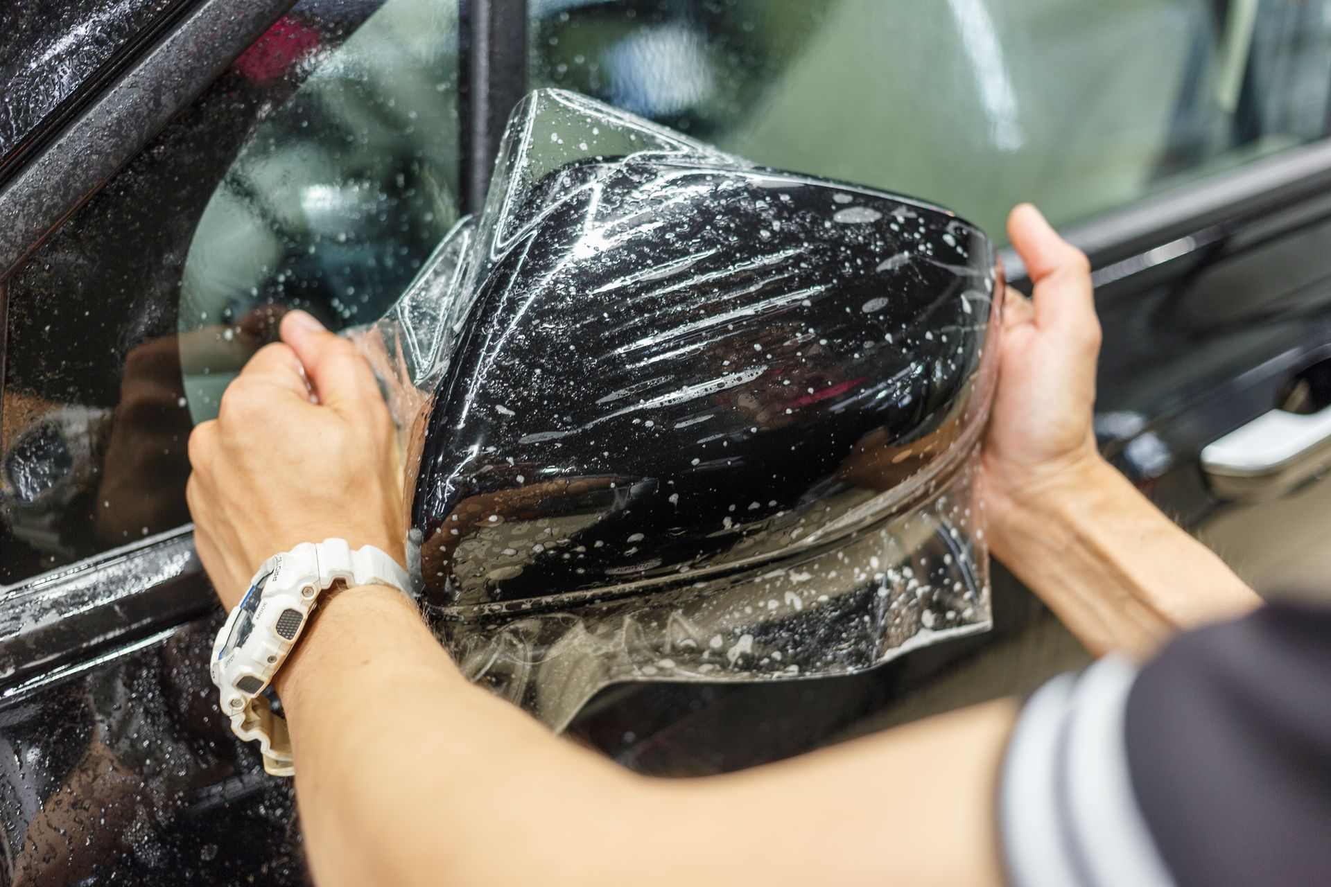 A person is applying tinted film to the side mirror of a car.
