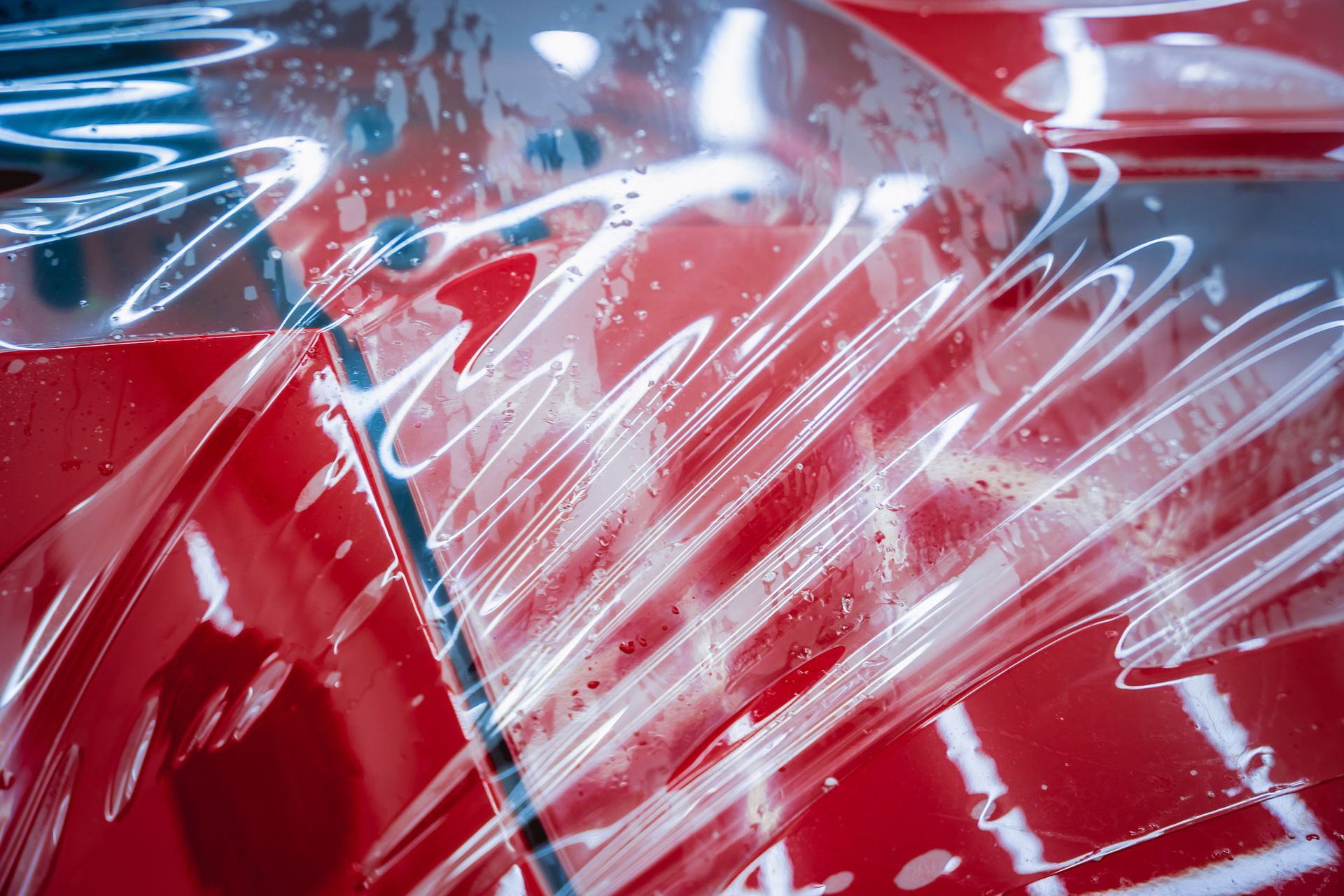 A close up of a red car covered in plastic wrap.