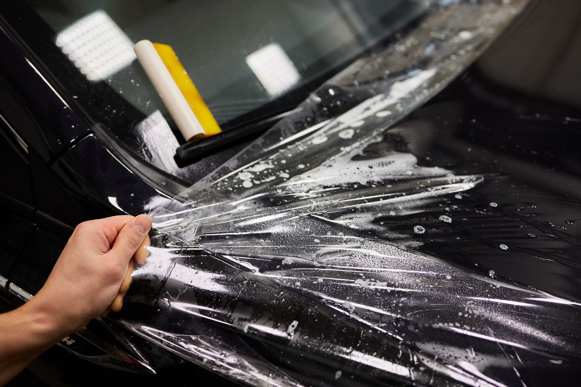 A person is applying a clear plastic film to a car.