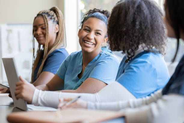 Four healthcare professionals in blue scrubs at a table, smiling and looking at each other, in a bright room.