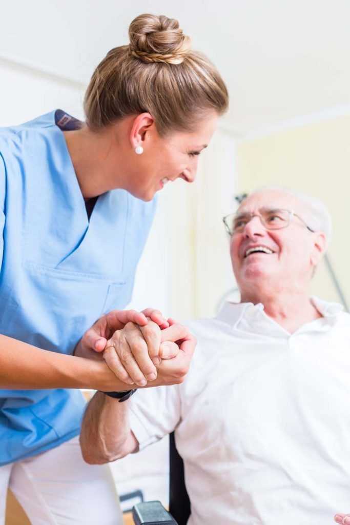 Woman in blue uniform assists elderly person, both smiling.