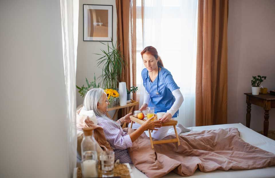 Nurse serving breakfast to a patient in bed; bedroom setting.