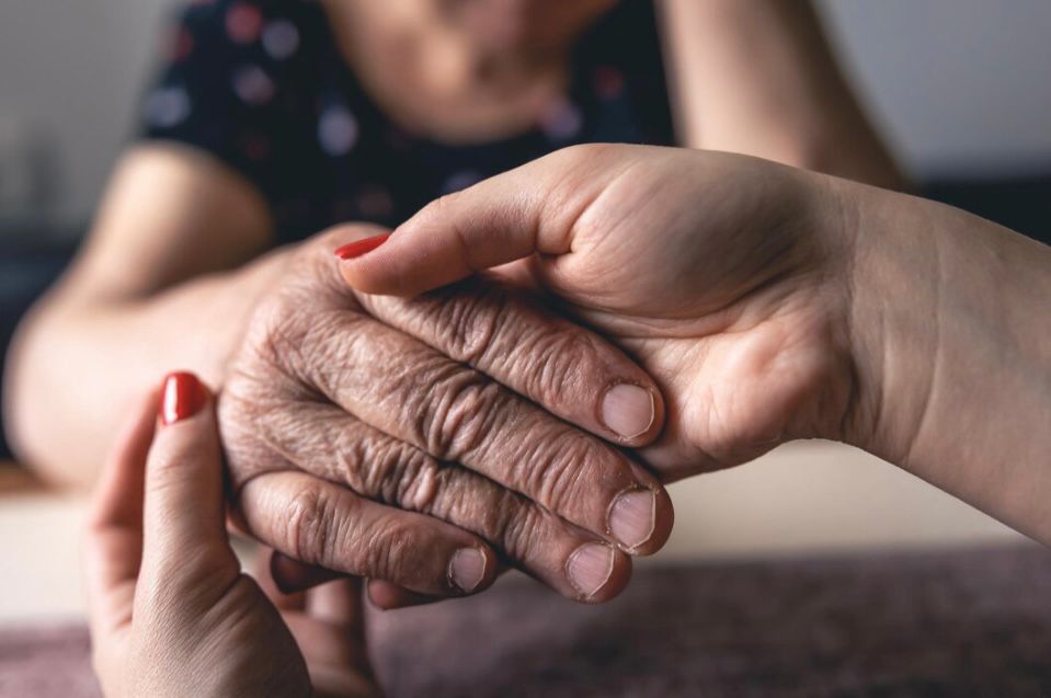 A younger person's hand gently holds an older person's hand, offering comfort and support.