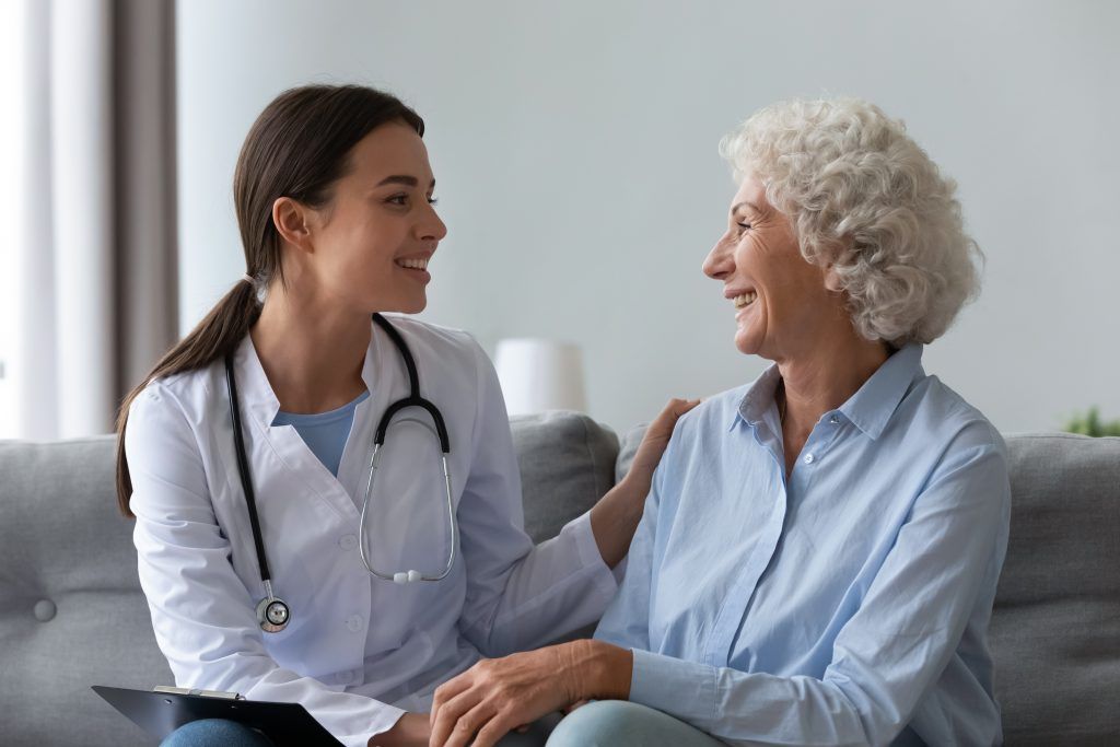 Doctor with stethoscope consults smiling patient in home setting.