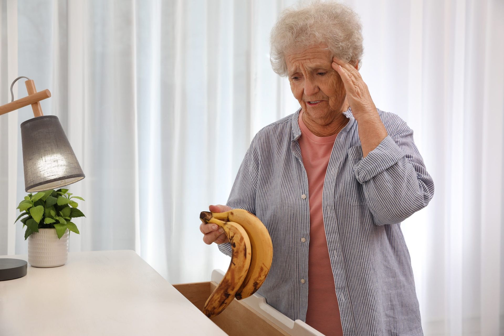Woman looking confused, holding bananas from a drawer, indoors.