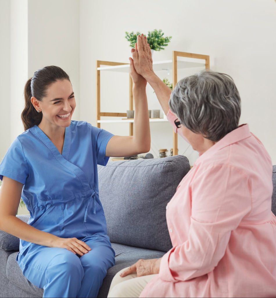 A healthcare worker and an older person giving each other a high-five on a sofa.