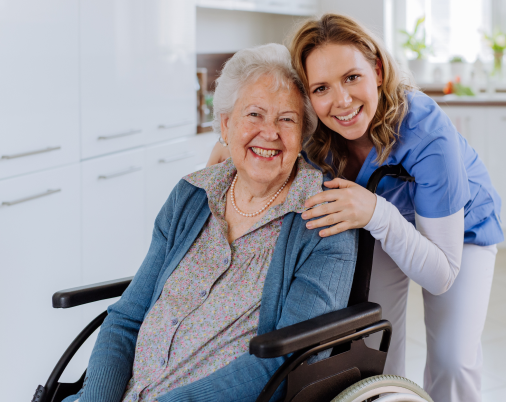 Woman in wheelchair smiling with caregiver, both indoors.