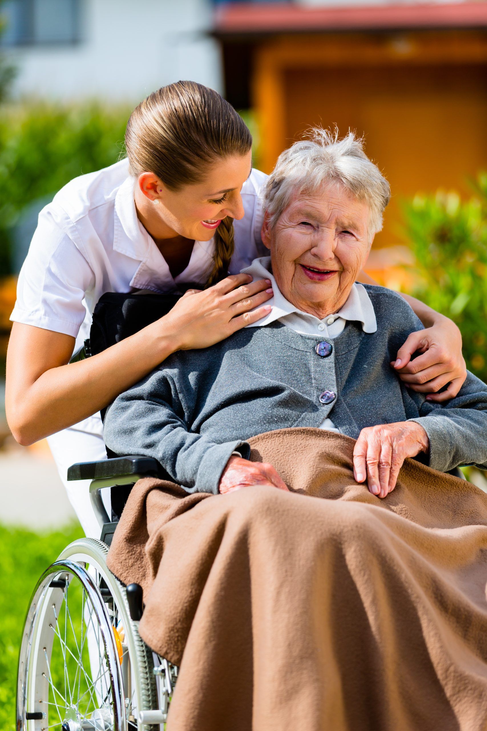 Caregiver comforts elderly person in wheelchair outdoors.