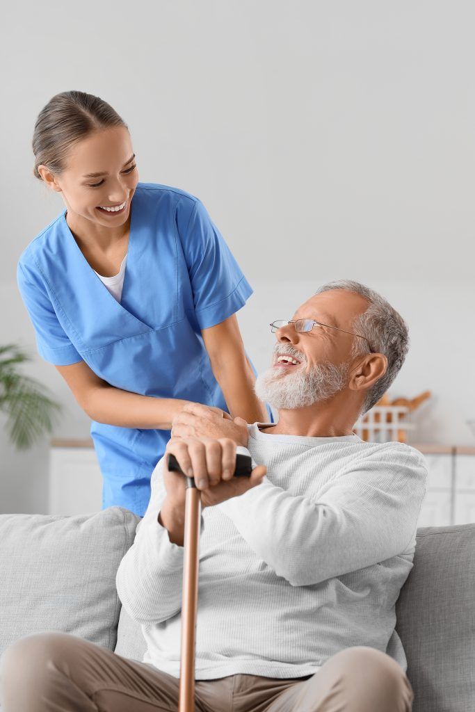 Woman in blue scrubs smiles at a seated man with a cane.