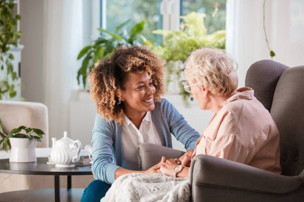 Woman comforts older person, holding hands, in a well-lit living room.