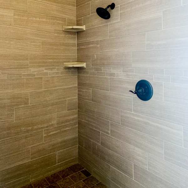 A shower with tiled walls and a blue shower head.