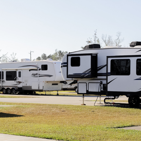 A white rv is parked next to another rv in a grassy area.