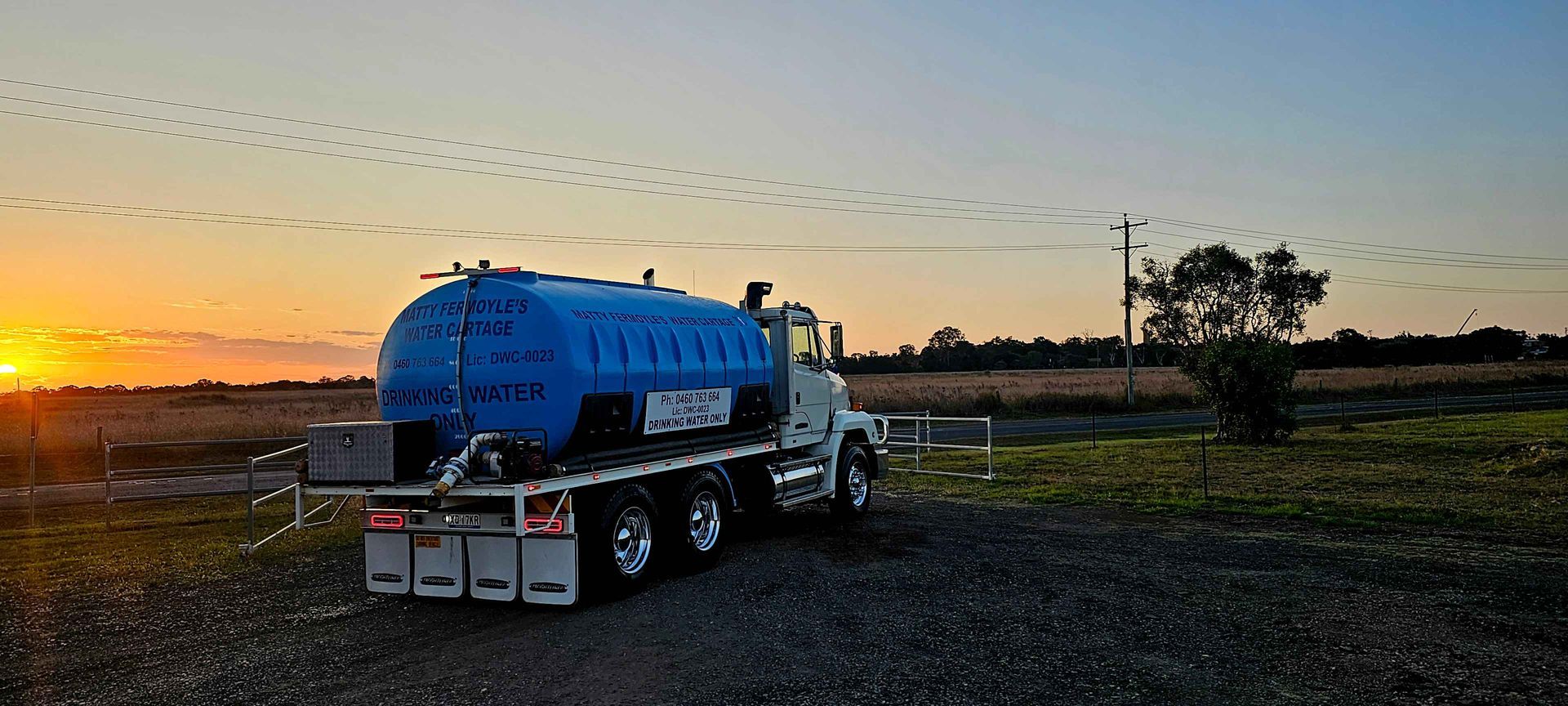 A blue tanker truck is parked in a gravel lot at sunset.