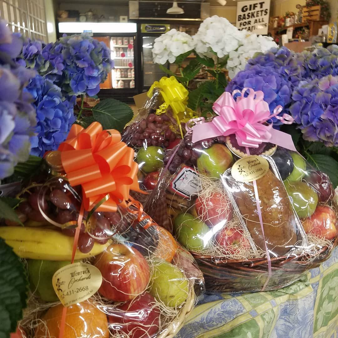 Fruit baskets wrapped in cellophane with bows, near blue and white hydrangeas.