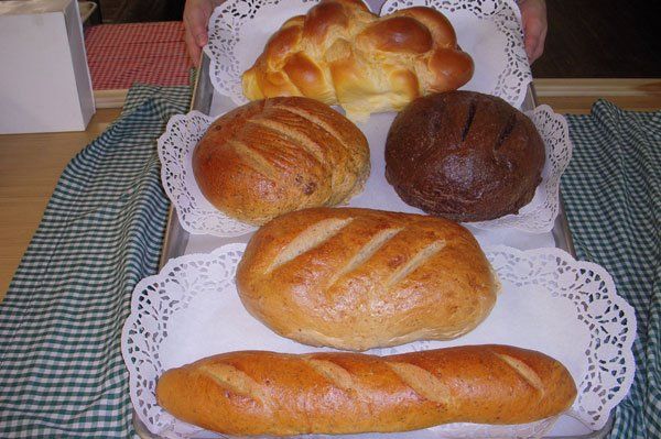 Various breads on trays with doilies, including challah, round loaves, and a baguette.