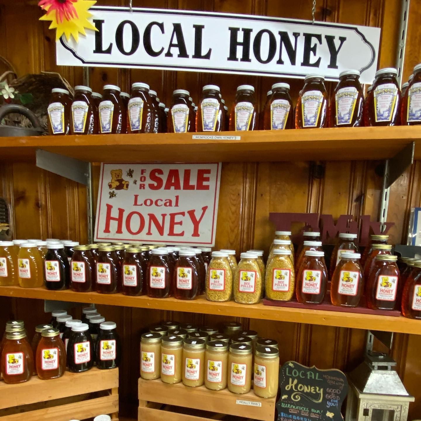 Shelves of various-sized jars filled with local honey, wooden setting, sale sign.