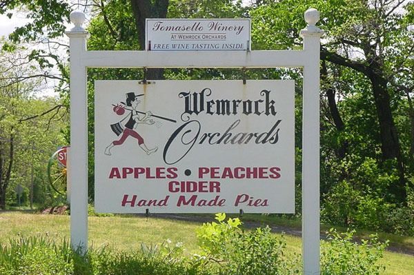 Sign for Wemrock Orchards: white, with black and red text, illustration of a person carrying a basket.