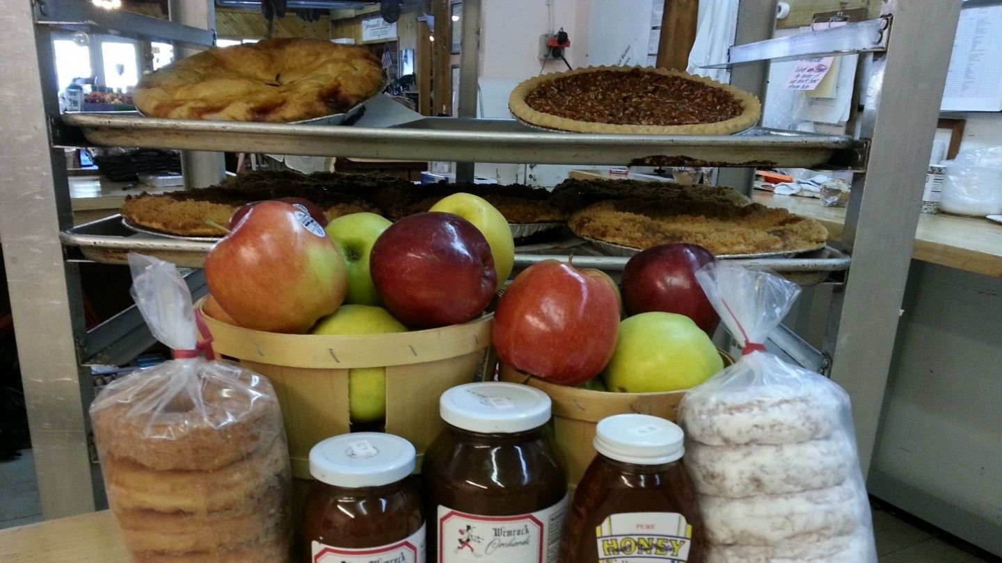 Fresh pies, apples, donuts, and jars of preserves on display in a bakery.