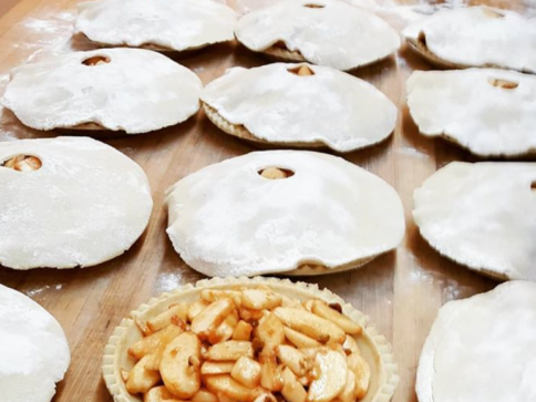 Raw apple pies with cut-out dough tops on a wooden surface, ready to bake.