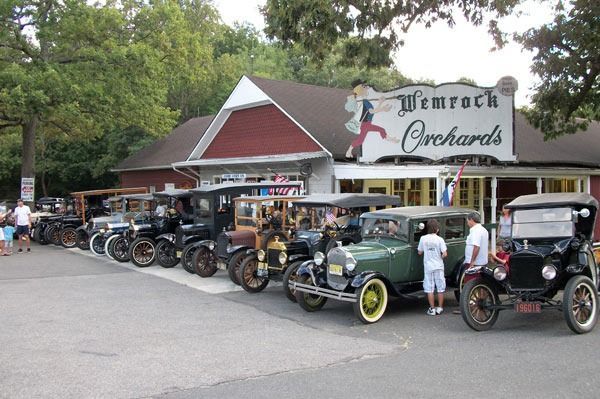 Vintage cars parked in front of Wemrock Orchards, with people milling about.