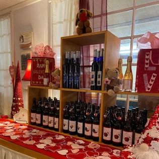 Display with wine bottles, Valentine's Day decor. Teddy bears, red and white hearts on a table.