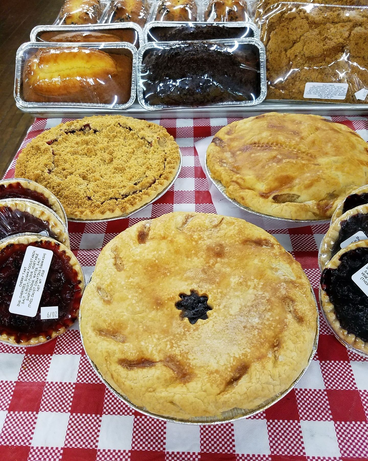 Display of baked goods, including pies and cakes on a red and white checkered tablecloth.