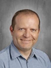 A man in a blue shirt is smiling for the camera.