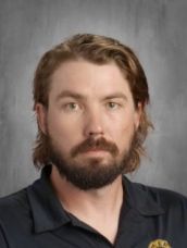 A man with a beard and long hair is wearing a black shirt.