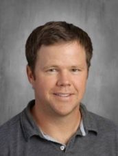 A man in a gray shirt is smiling for the camera.