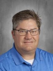 A man wearing glasses and a blue shirt is smiling for the camera.