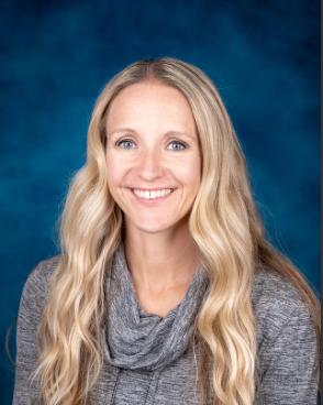 A woman with long blonde hair is wearing a gray sweater and smiling for the camera.