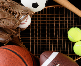 A bunch of sports balls including a basketball a football a tennis racket and a baseball glove